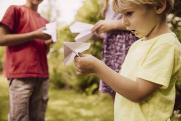 Drei Kinder spielen mit Papierfliegern im Garten - MFF001878