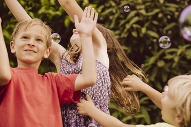 Drei Kinder spielen mit Seifenblasen im Garten - MFF001883