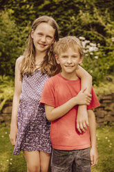 Smiling girl putting arm around brother in garden - MFF001886