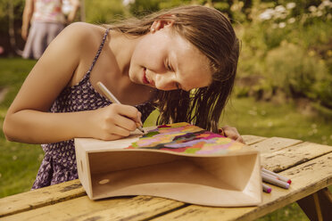 Mädchen zeichnet auf einem hölzernen Zeitschriftenordner im Garten - MFF001949