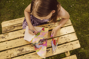 Mädchen zeichnet auf einem hölzernen Zeitschriftenordner im Garten - MFF001887