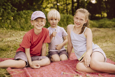 Drei Kinder sitzen auf einer Decke auf einer Wiese - MFF001916