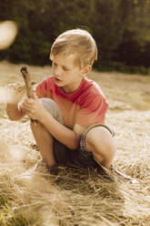 Boy carving a piece of wood on field - MFF001952