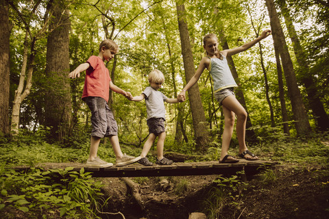 Drei Kinder balancieren auf einer kleinen Brücke im Wald, lizenzfreies Stockfoto