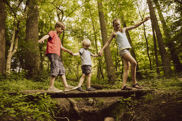 Three children balancing along a small bridge in forest - MFF001931