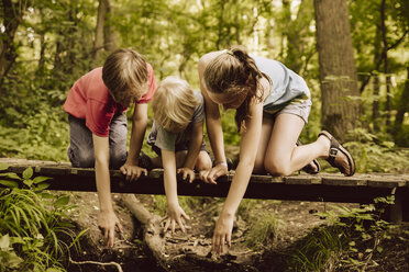 Three children reaching down from a small bridge in forest - MFF001953