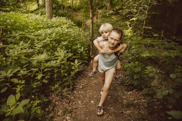 Mädchen trägt kleinen Jungen huckepack durch einen Wald - MFF001934