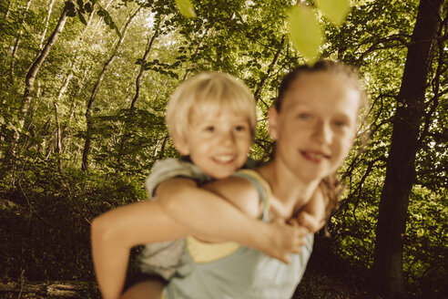 Mädchen trägt kleinen Jungen huckepack durch einen Wald - MFF001936