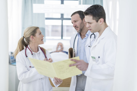 Drei Ärzte mit Bericht in einem Krankenhauszimmer, lizenzfreies Stockfoto