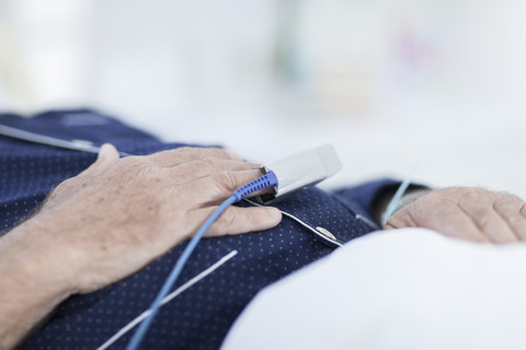 Hände eines Patienten mit Herzfrequenzmessgerät am Finger im Krankenhausbett liegend, Nahaufnahme, lizenzfreies Stockfoto