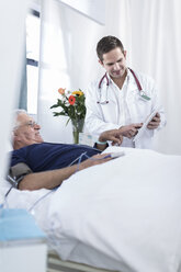 Arzt zeigt älteren Mann im Krankenhausbett liegend etwas auf einem digitalen Tablet - ZEF006247