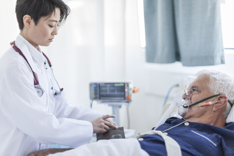 Arzt misst den Blutdruck eines älteren Mannes mit Sauerstoffmaske in einem Krankenhaus, lizenzfreies Stockfoto
