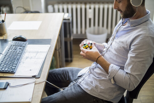 Junger Mann im Büro am Schreibtisch mit Rubik's Cube - FKF001201