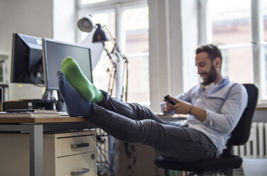 Junger Mann im Büro mit Füßen auf dem Schreibtisch und verschiedenen Socken - FKF001202