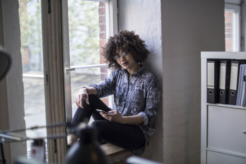 Young woman in office sitting at the window - FKF001313