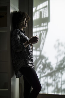 Young woman with cup of coffee leaning against cabinet - FKF001209