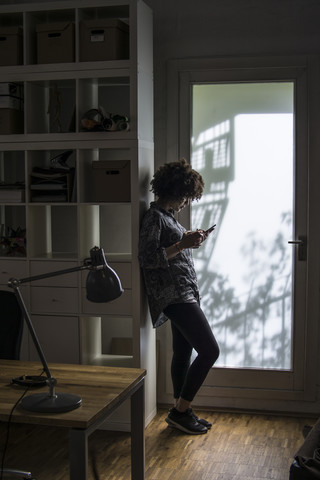 Junge Frau mit Handy an Schrank gelehnt, lizenzfreies Stockfoto