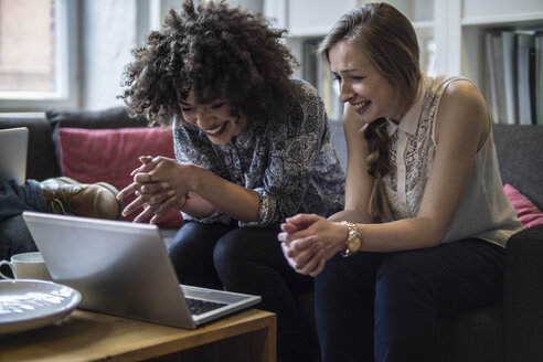 Zwei glückliche junge Frauen teilen sich einen Laptop - FKF001319