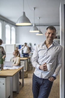 Smiling man in office with colleagues in background - FKF001213