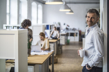 Lächelnder Mann im Büro mit Kollegen im Hintergrund - FKF001214