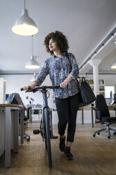 Junge Frau schiebt Fahrrad im Büro - FKF001320