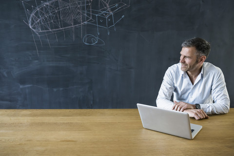 Smiling mature mman with laptop at blackboard stock photo