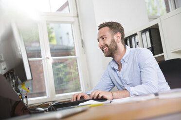 Smiling young man in office working on computer - FKF001233