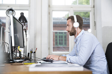 Young man in office wearing headphones working on computer - FKF001234