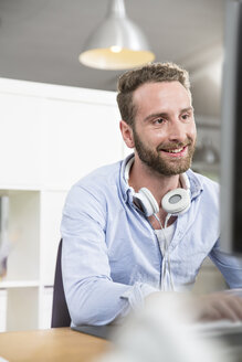 Lächelnder junger Mann im Büro am Schreibtisch bei der Arbeit am Computer - FKF001235