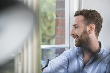 Lächelnder junger Mann, der aus dem Fenster schaut - FKF001325