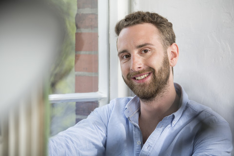 Porträt eines lächelnden jungen Mannes am Fenster, lizenzfreies Stockfoto