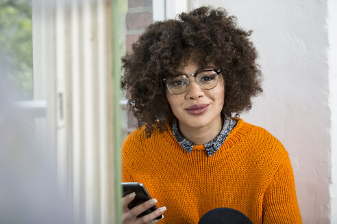 Portrait of smiling young woman with cell phone at the window - FKF001241