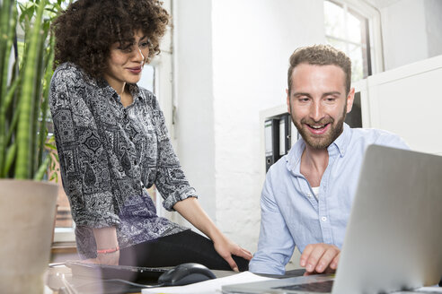 Smiling man and woman in office sharing laptop - FKF001250