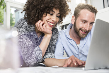 Smiling man and woman in office sharing laptop - FKF001252