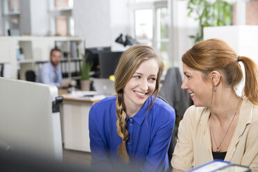 Zwei lächelnde Frauen im Büro schauen sich an - FKF001255