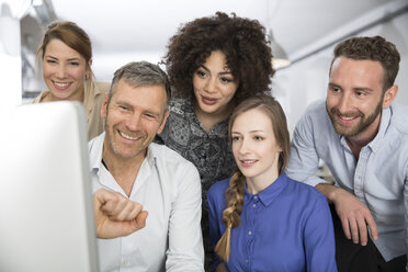 Smiling colleagues in office looking at monitor - FKF001260