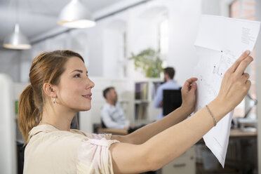 Smiling woman in office looking at plan - FKF001267