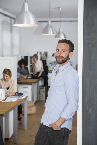 Smiling man in office with colleagues in background stock photo