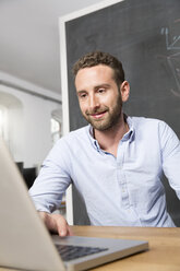 Junger Mann im Büro mit Laptop - FKF001336