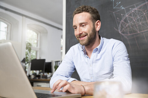 Junger Mann im Büro mit Laptop - FKF001299