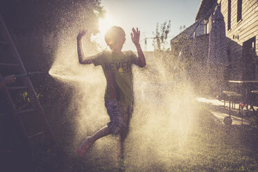 Junge und Mädchen haben Spaß mit spritzendem Wasser im Garten - SARF002062