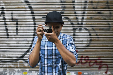 Junger Mann mit Baseballmütze beim Fotografieren vor einem Rollladen - EBSF000785