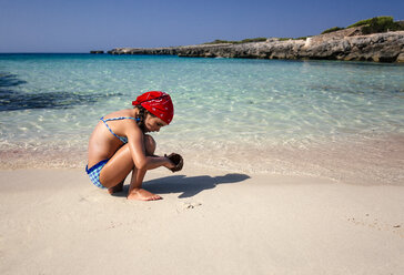 Spanien, Balearen, Menorca, kleines Mädchen spielt am Strand mit einer Kokosnussschale - MGOF000325