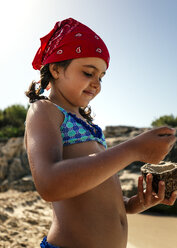 Spanien, Balearen, Menorca, kleines Mädchen spielt am Strand mit einer Kokosnussschale - MGOF000330