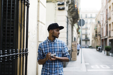 Spain, Barcelona, young man with baseball cap and camera on the street - EBSF000789