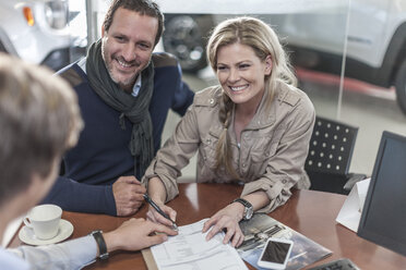 Couple signing sales contract at car dealership - ZEF006912