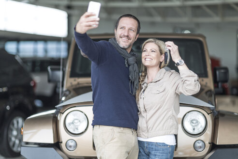 Glückliches Paar im Autohaus, das ein Selfie vor seinem neuen Auto macht - ZEF006922