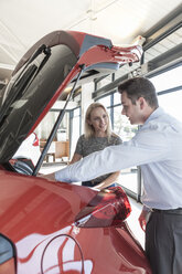 Car dealer explaining new car to young woman - ZEF006929