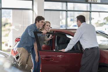 Autohändler zeigt einem jungen Paar im Ausstellungsraum ein neues Auto - ZEF006932