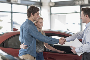 Autohändler und junges Paar beim Händeschütteln im Ausstellungsraum - ZEF006933